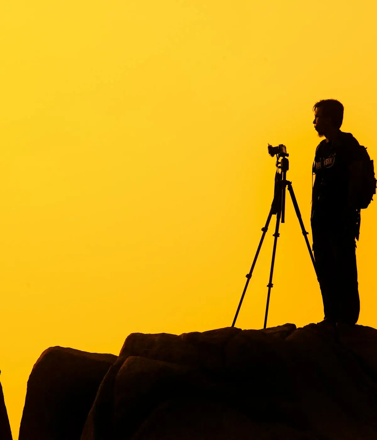 Silhouette eines Fotografen mit Stativ vor orangefarbenem Abendhimmel